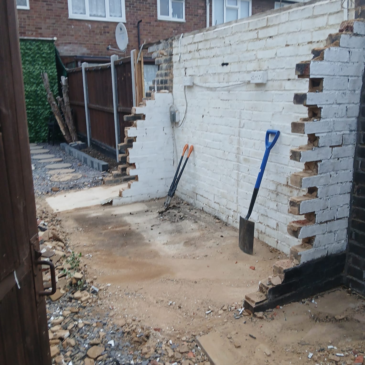 White brick garage walls partly taken down with a shovel and debris on the ground