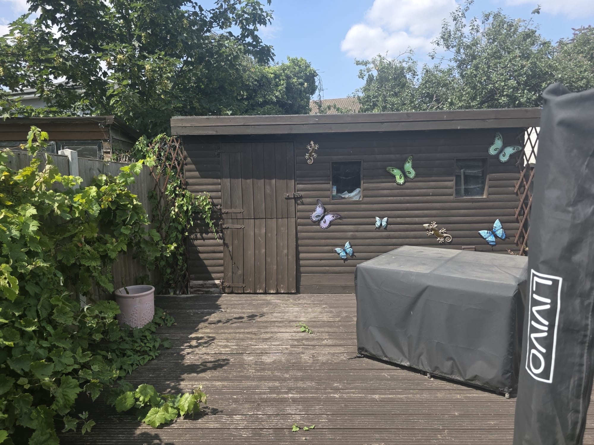 Timber shed with decorated panels standing on a decked garden in Essex