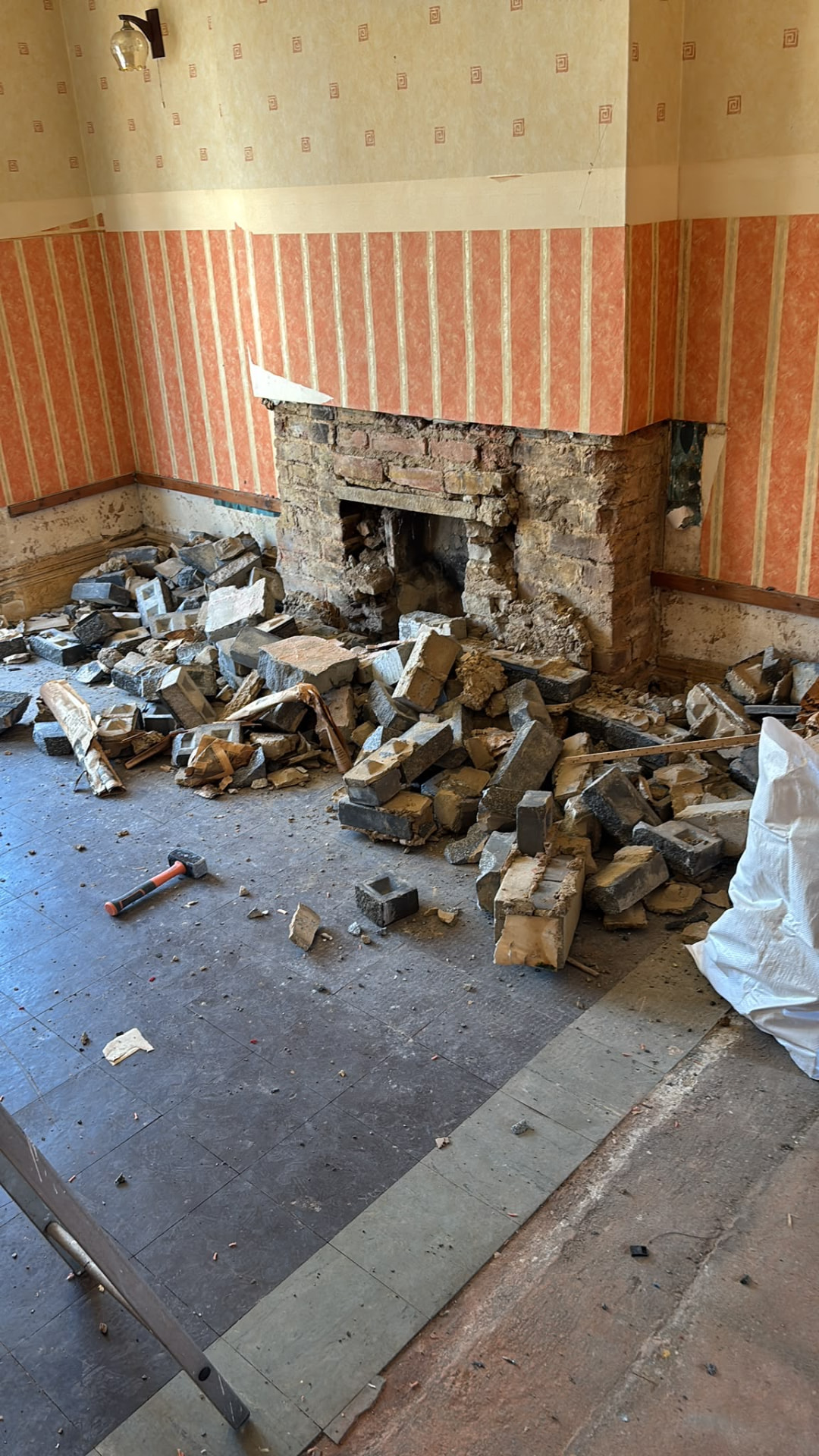 Brick fireplace partly taken down with demolition rubble across the room floor