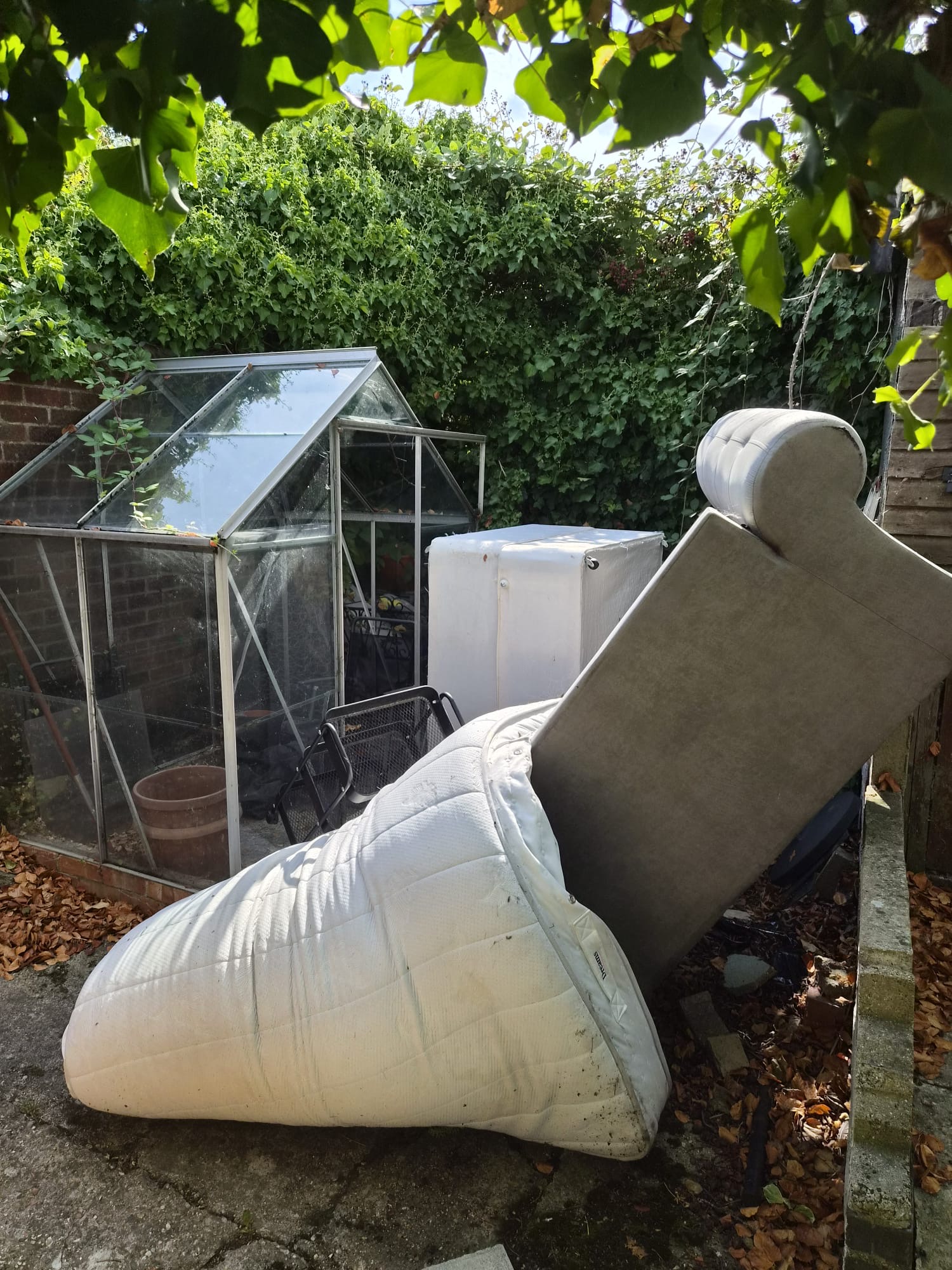 Glass greenhouse garden with a mattress, sofa and fridge waiting for collection in Essex